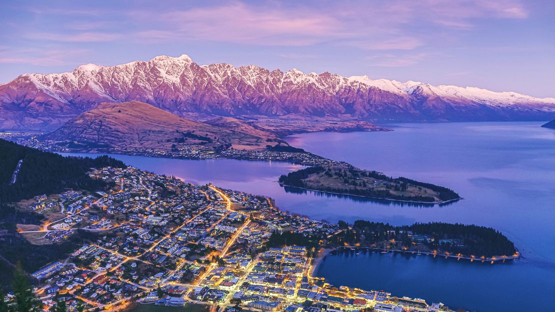 Twilight view of a lakeside town with illuminated streets against snow-capped mountains in New Zealand