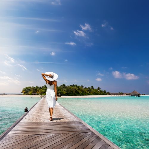 Woman in white dress and hat walking on a jetty in the Maldives.