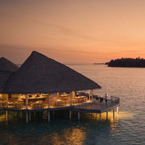 Overwater bungalows at sunset with warm lights and distant island.