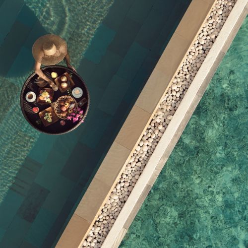 Person with a hat enjoying a floating breakfast in a pool.