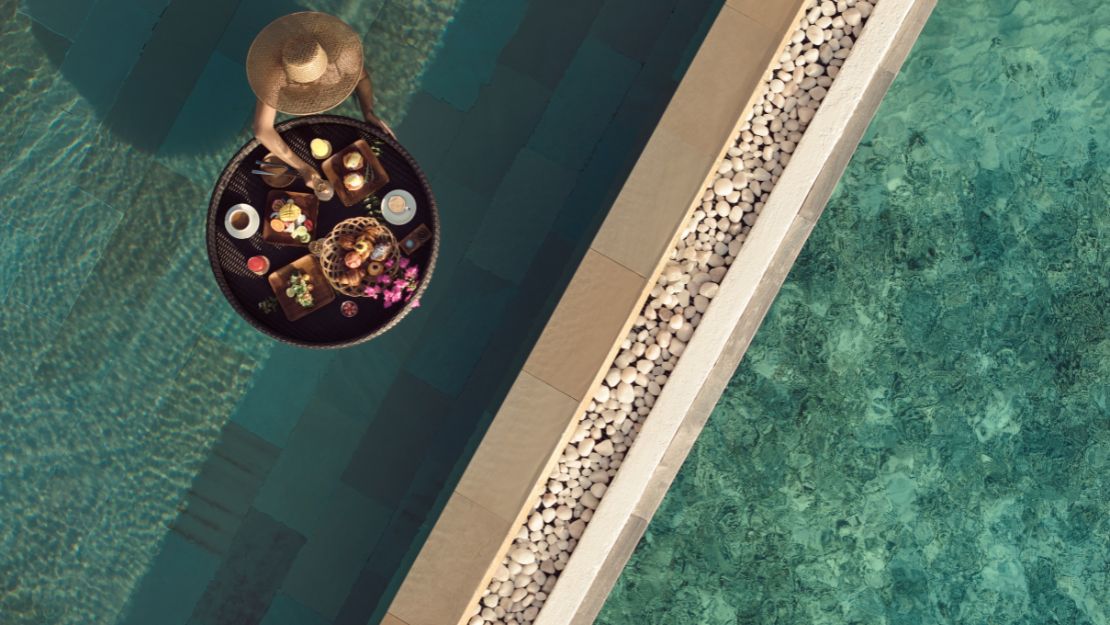 Person with a hat enjoying a floating breakfast in a pool.