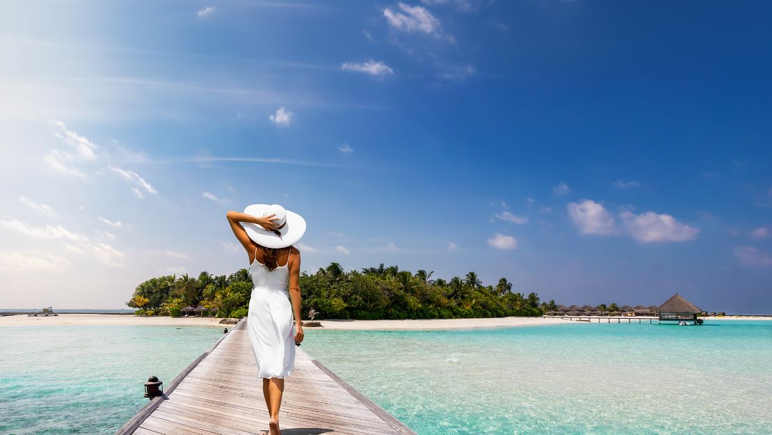 Woman in white dress and hat walking on a jetty in the Maldives.