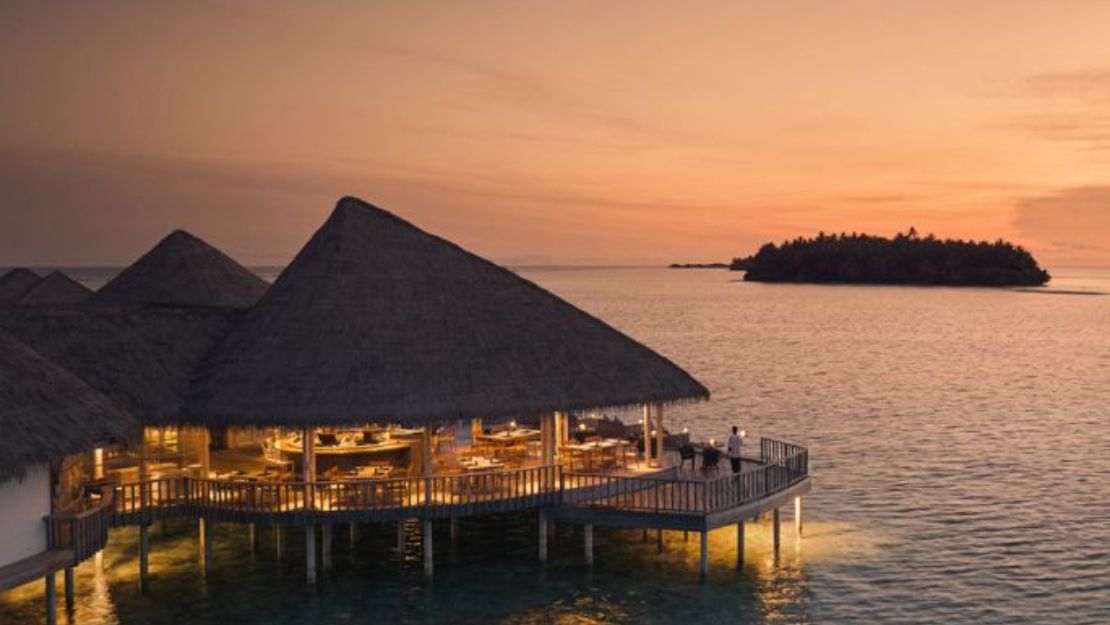 Overwater bungalows at sunset with warm lights and distant island.