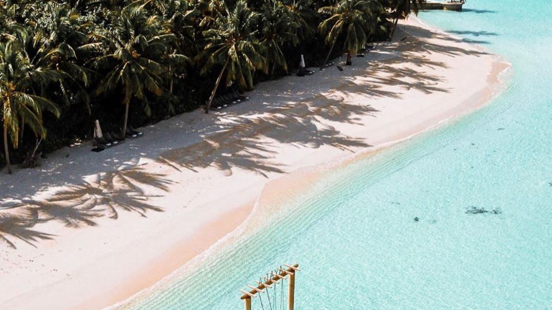 Tropical beach with clear blue water, white sand, and palm trees.