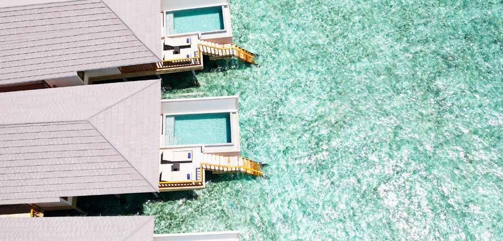 Overhead view of overwater bungalows with private pools above a turquoise sea.