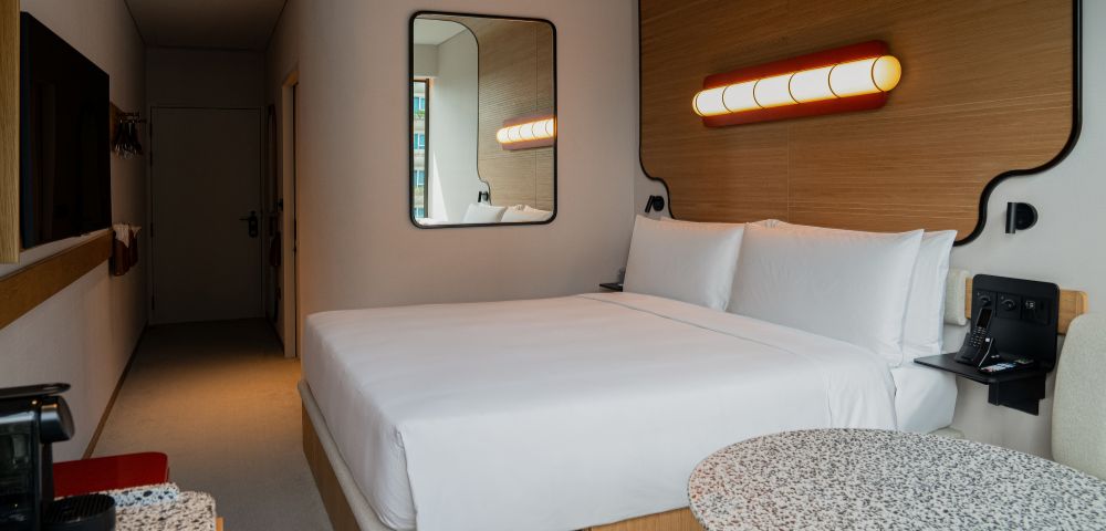 Modern hotel room with a double bed, wooden walls, a mirror, and chic lighting.