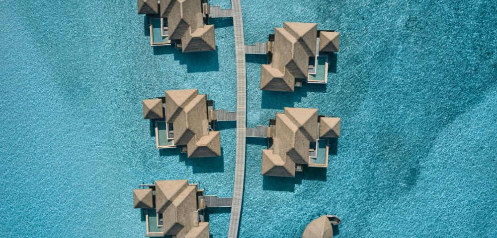 Aerial view of overwater bungalows with thatched roofs above a turquoise sea.