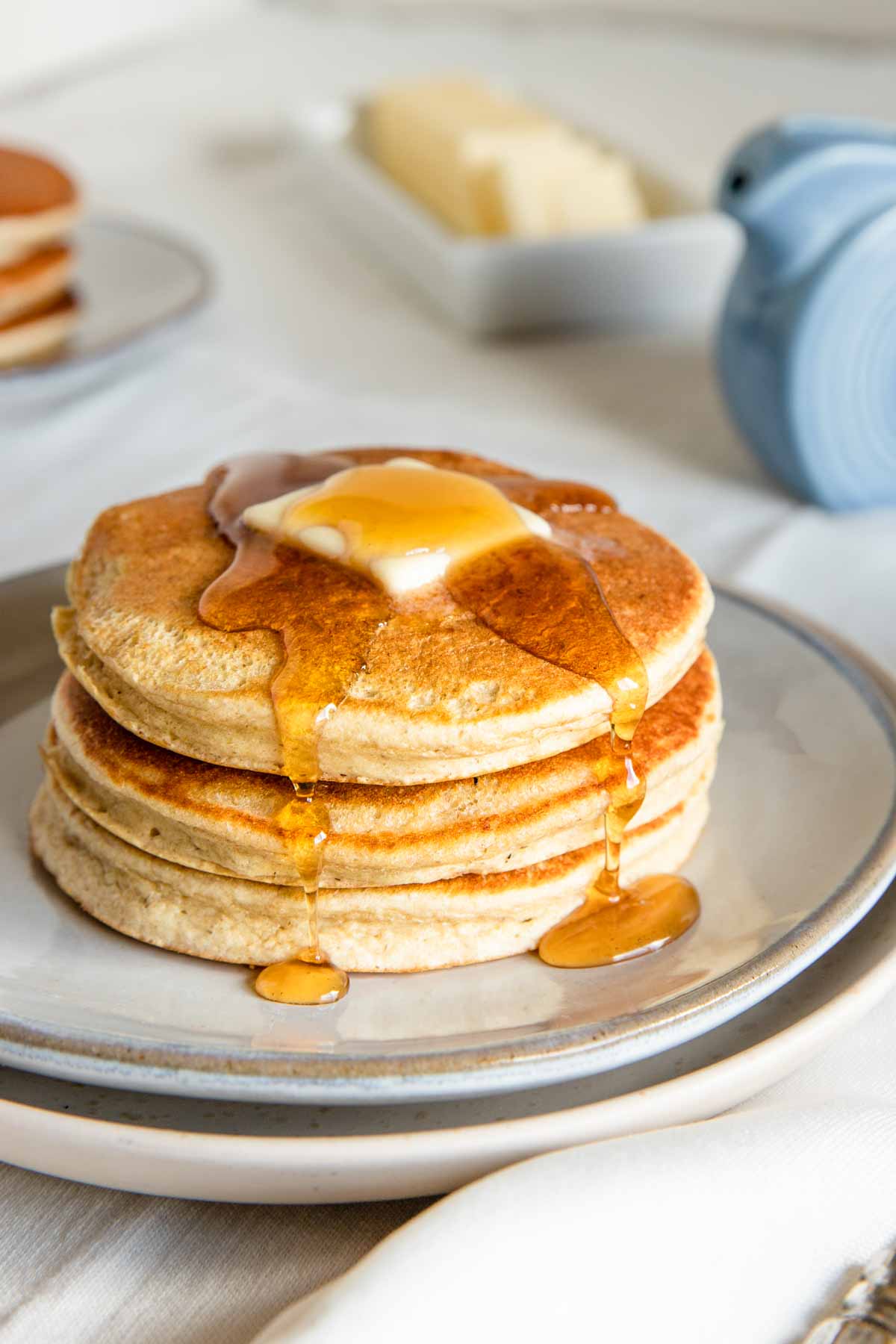 fluffy pancakes on a ceramic plate with a butter pat and syrup drips