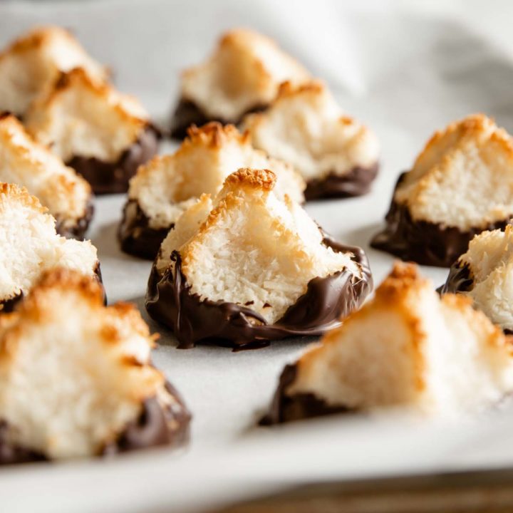 recipe card featured mage of coconut macaroons sitting on parchment and dipped in chocolate