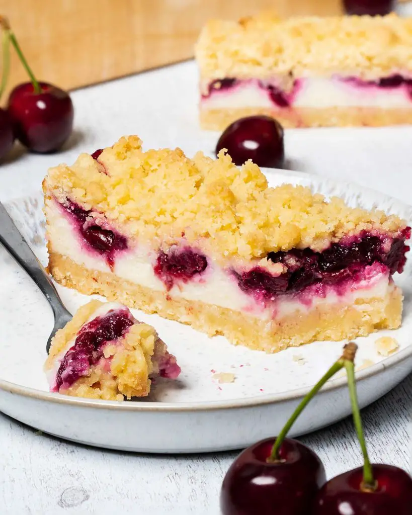 Cherry cheesecake bars. Delicious shortbread, creamy eggless baked cheesecake and rich cherry pie filling topped with more shortbread crumbs. This is one cheesecake no one can turn down! Recipe by movers and bakers