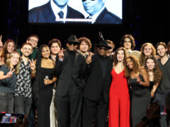 A group of college-aged students gather on stage after a performance.