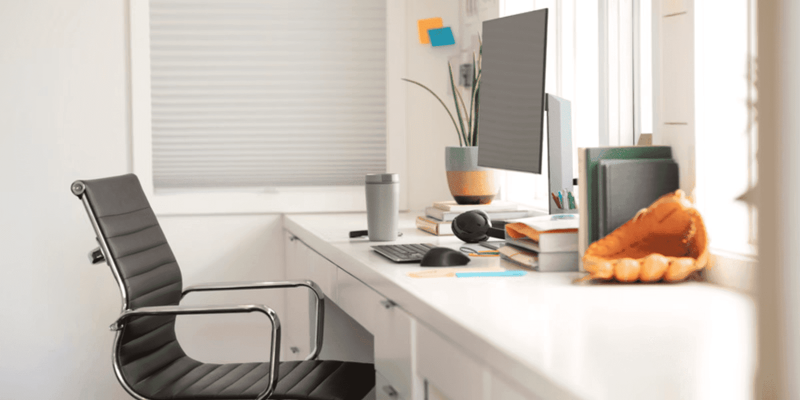 Espacio de trabajo moderno con escritorio blanco, silla ergonómica gris, monitor, teclado y elementos decorativos