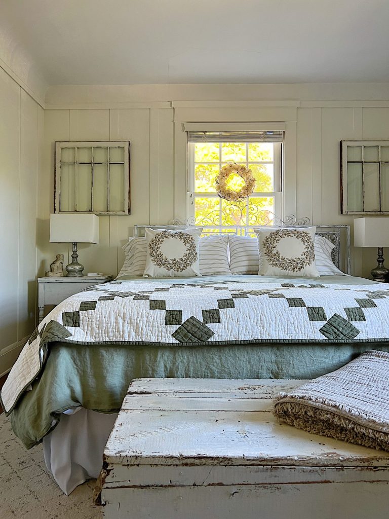 small bedroom with green linen duvet, green and white patchwork quilt, pillows and a nightstand on each side.