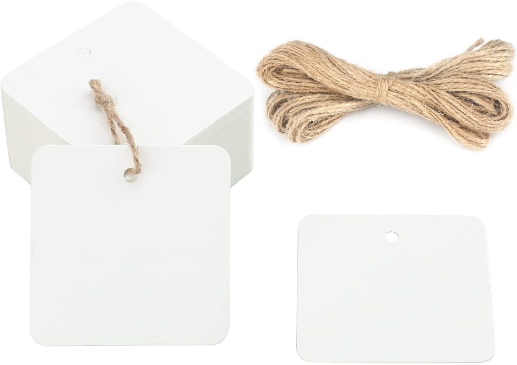 A stack of blank square tags, perfect for gift wrapping, with one tied by twine, sits next to an untied bundle of twine.