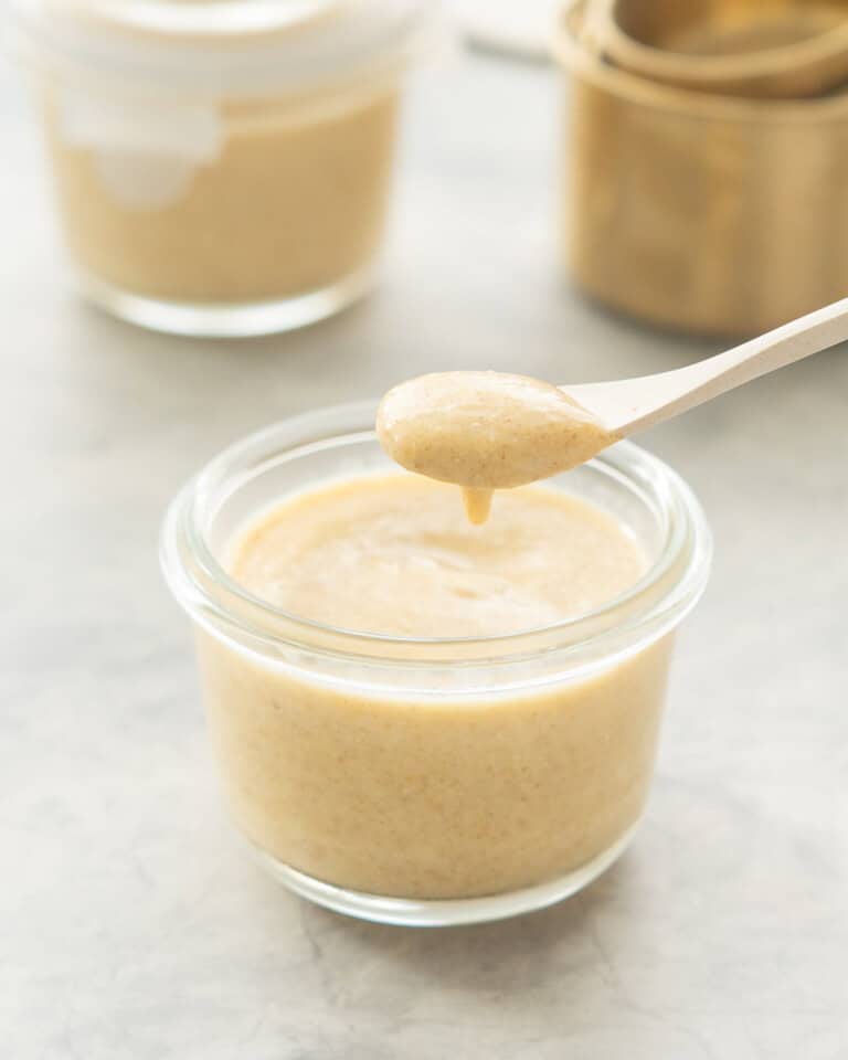 A small glass jar of peach pudding with a spoonful being scooped out of it.