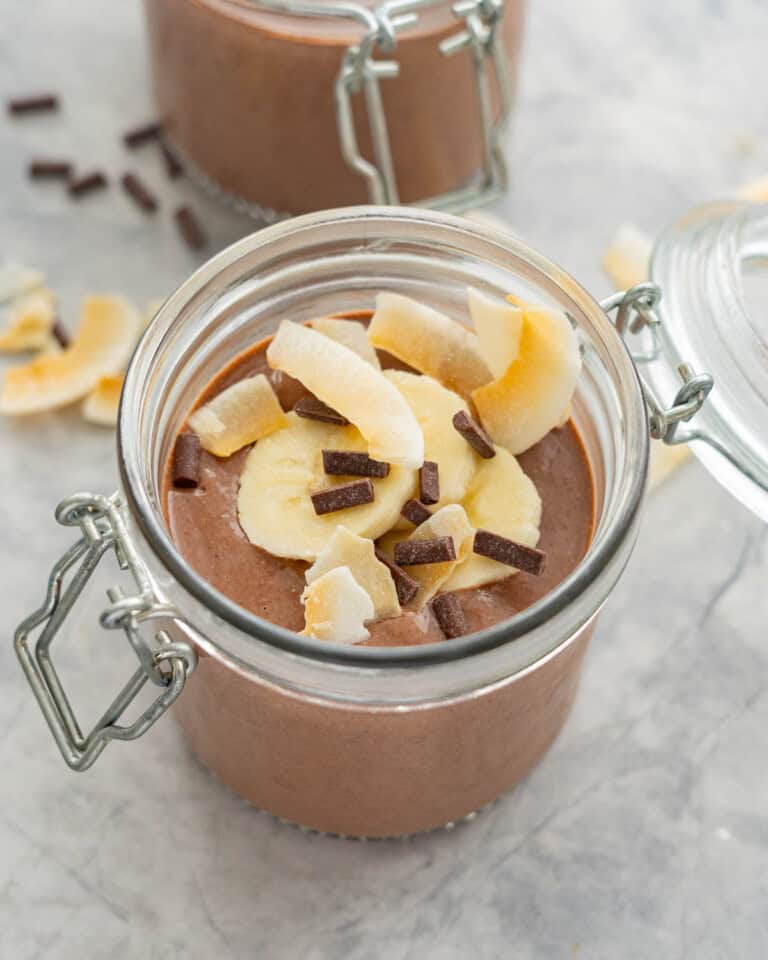 A chocolate pudding in a jar topped with banana slices, coconut chips and chocolate chips.