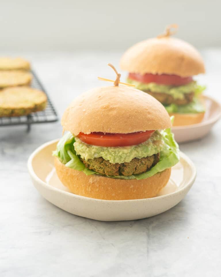 Burger on a plate with lettuce, chickpea patty, guacamole, slice of tomato and top of burger.