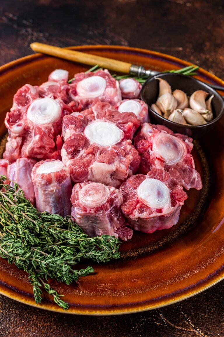 Fresh uncooked beef Oxtail cut Meat on rustic plate with herbs. Dark background. Top view