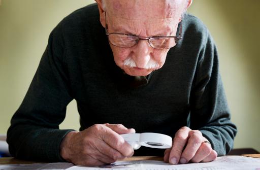 man looking at paper through a magnifying glass.