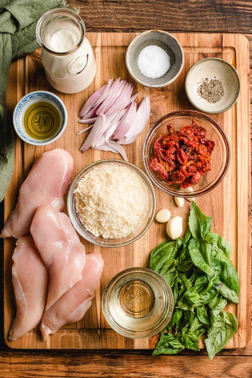 Ingredients for sun dried tomato chicken pasta displayed on a wooden cutting board.