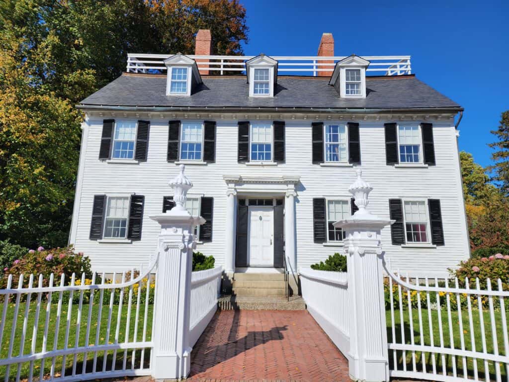 facade of a white colonial house with pillaredgate and bricked walkway leading to the front door.