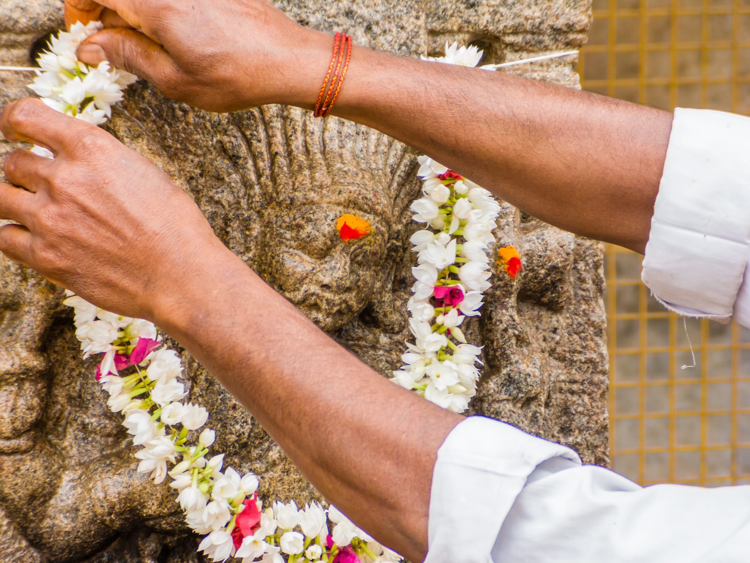 A Hindu offers a flowered garland to a god carved on a stone pillar at the the temple of Shiva in Nanjangud, South India.