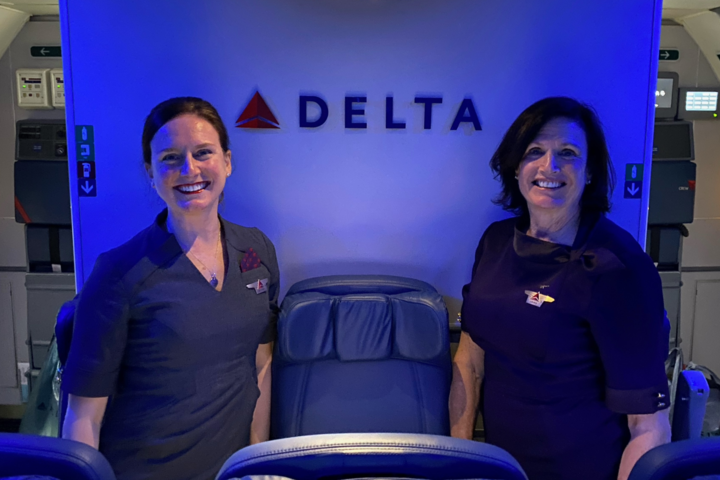 A mother and daughter duo who have nearly 30 years of combined service at Delta pose for a photo onboard a plane.