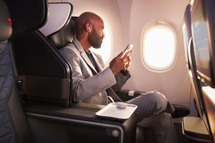 A Delta customer sits in Delta's First Class cabin, holding their phone.