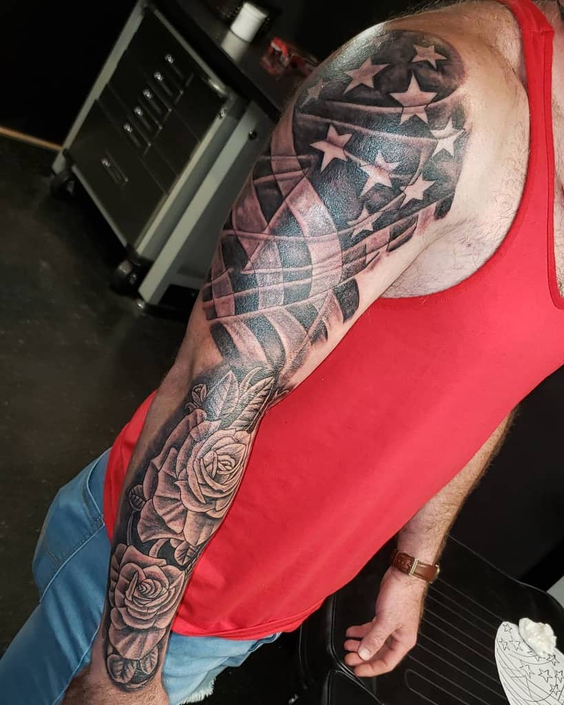 American flag full-sleeve tattoo combining bold stars and stripes with detailed roses, blending patriotism and elegance in black and grey shading