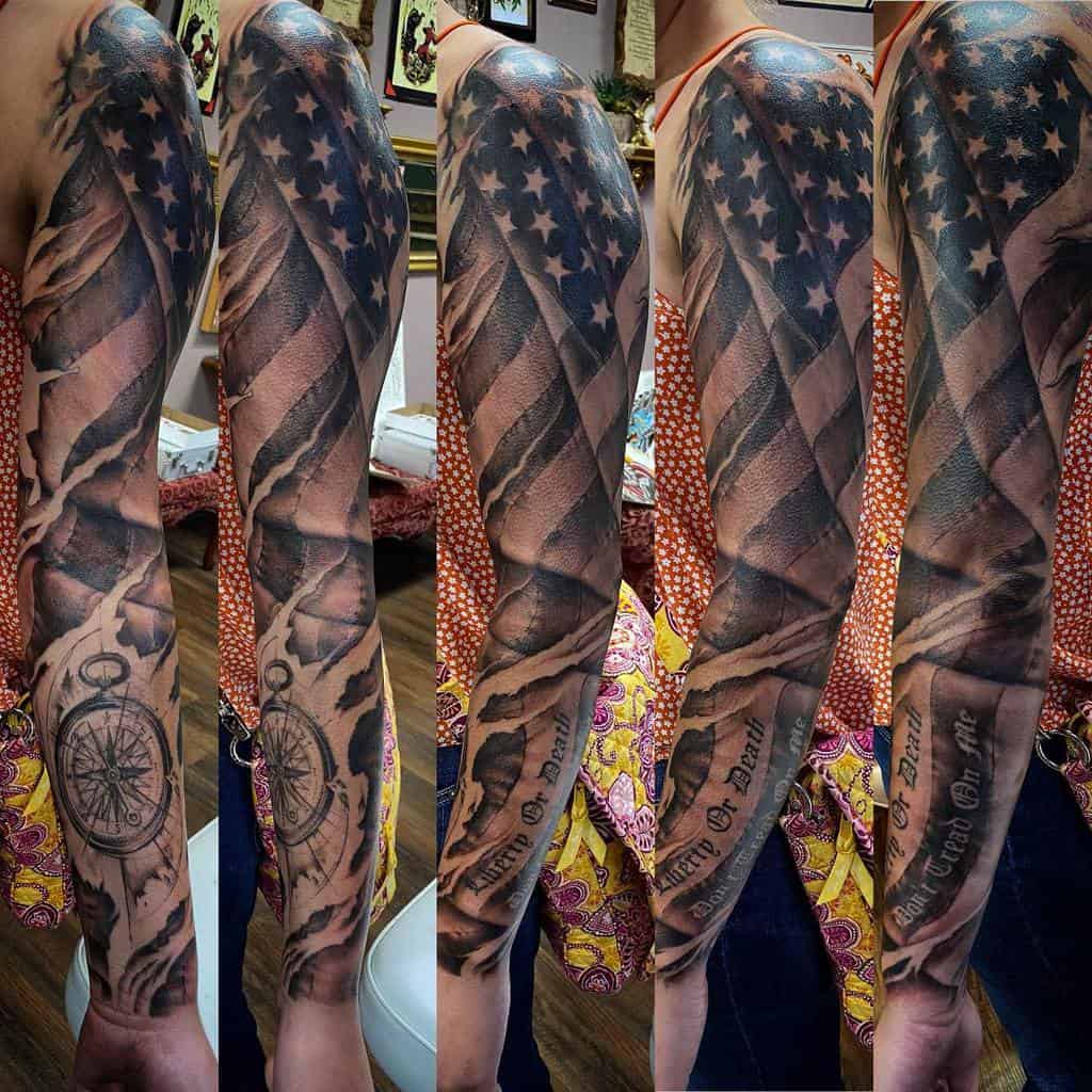 Dynamic full-sleeve tattoo featuring a weathered American flag wrapped around the arm, paired with intricate compass and text elements for a personalized touch