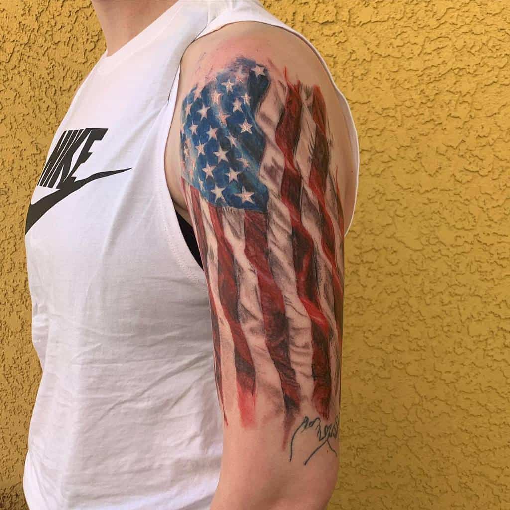 Tattoo of a tattered American flag on a man's upper arm