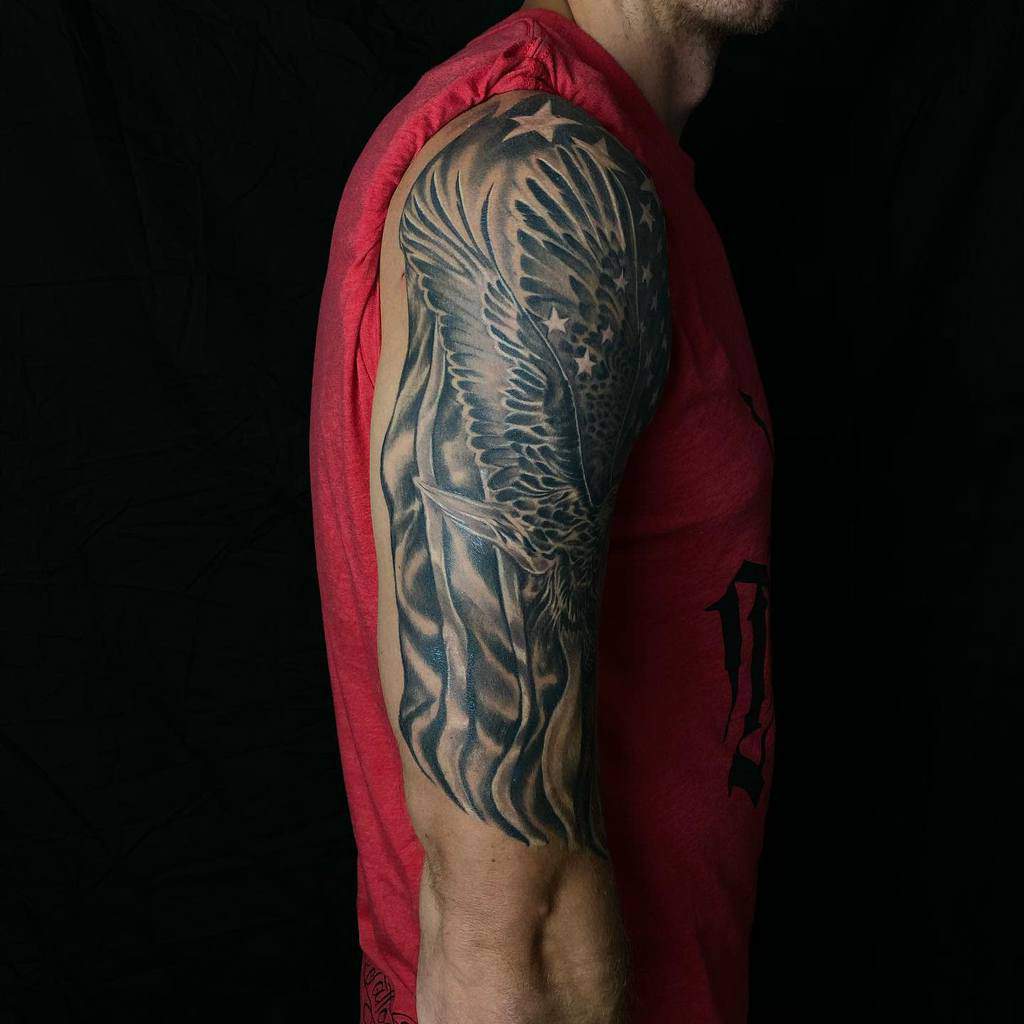 Dynamic upper-arm tattoo showcasing a detailed bald eagle in flight, its feathers blending seamlessly with a flowing American flag, creating a bold and patriotic design