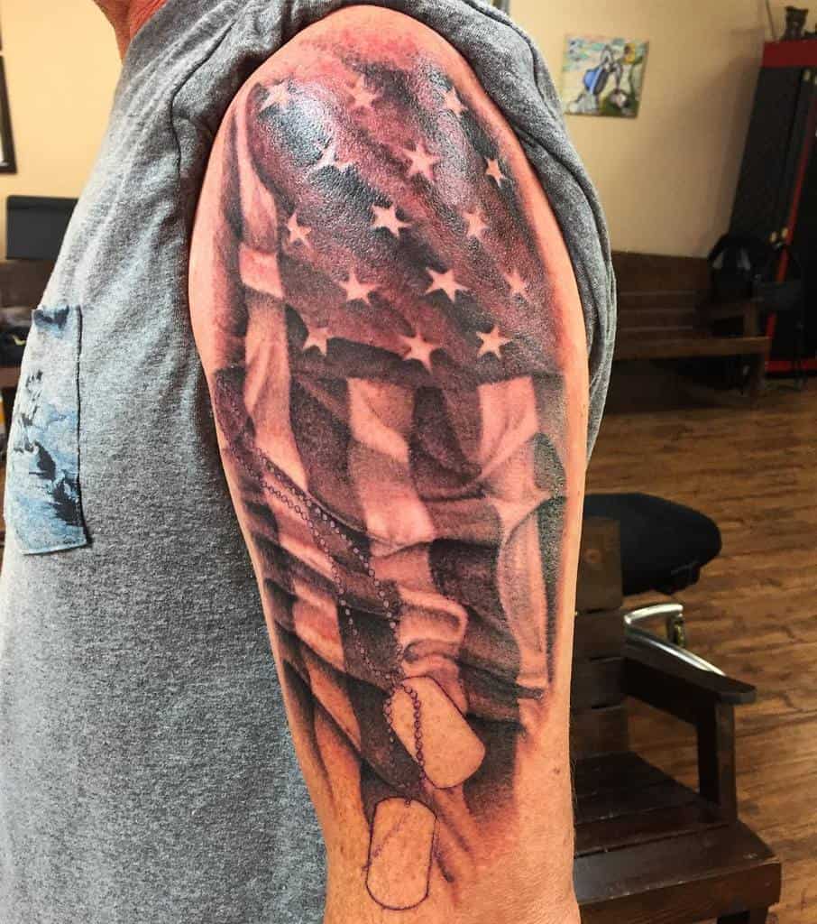 Tattoo of an American flag and dog tags on a person's upper arm