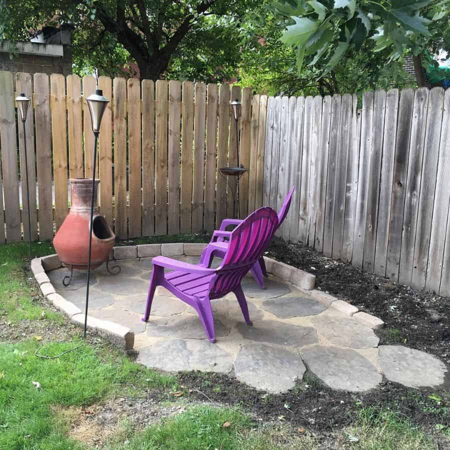 small corner stone patio with fire pit and purple plastic chairs 