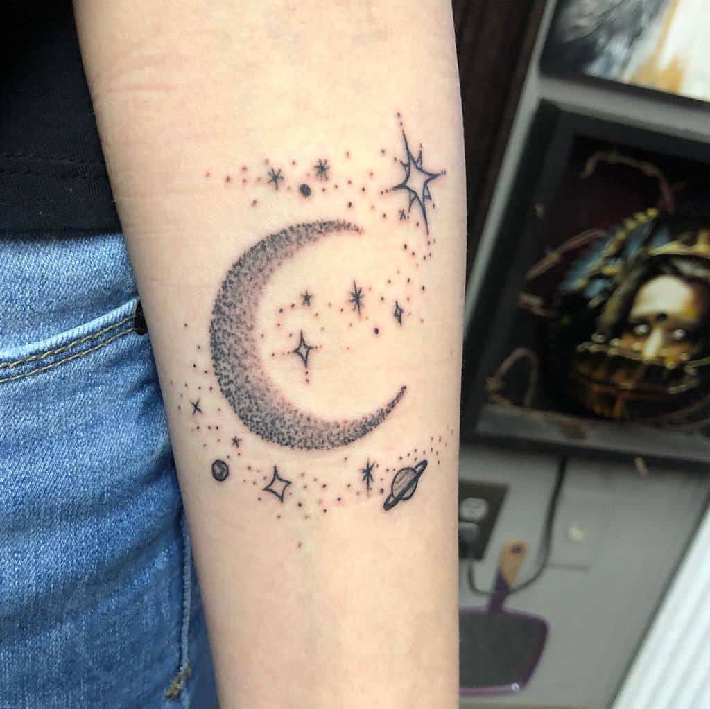 Crescent moon, shimmering stars, and distant planets tattoo on a forearm