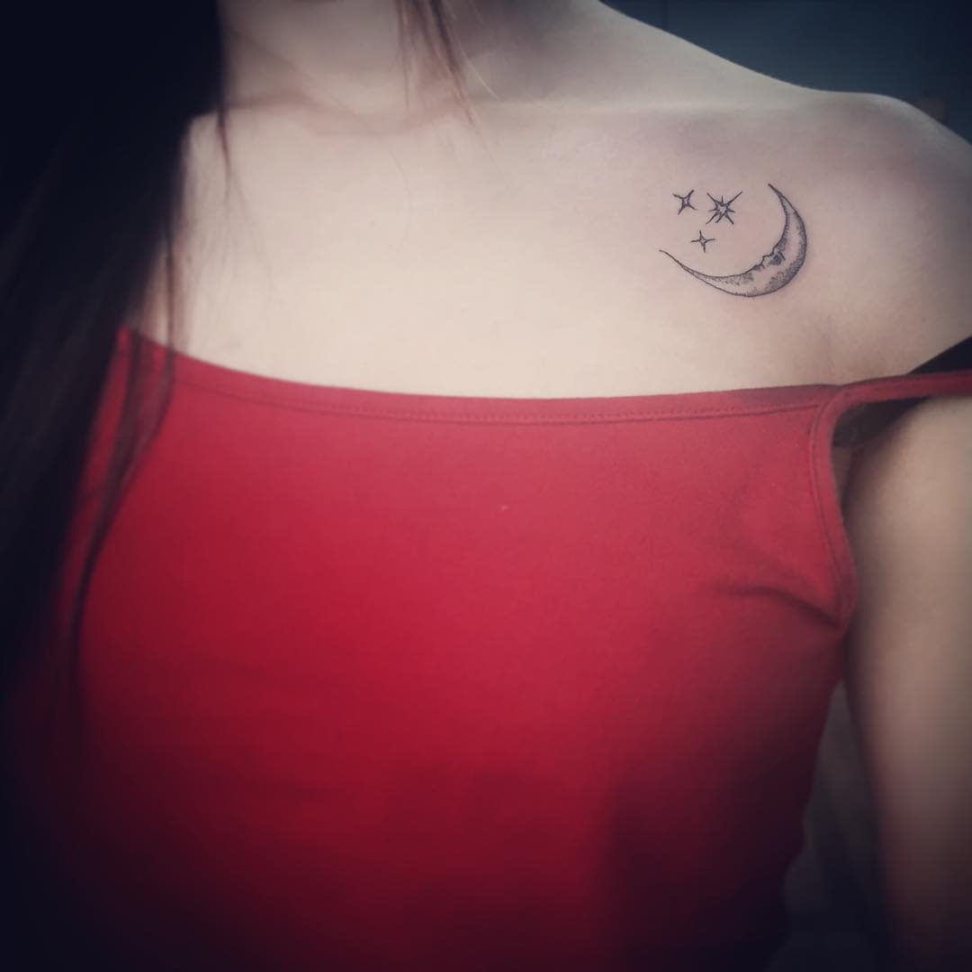 Person with a crescent moon and stars tattoo on their collarbone, wearing a red off-shoulder top