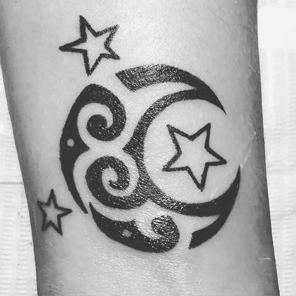 Black and white tattoo with stars, spirals, and a shimmering moon on the skin