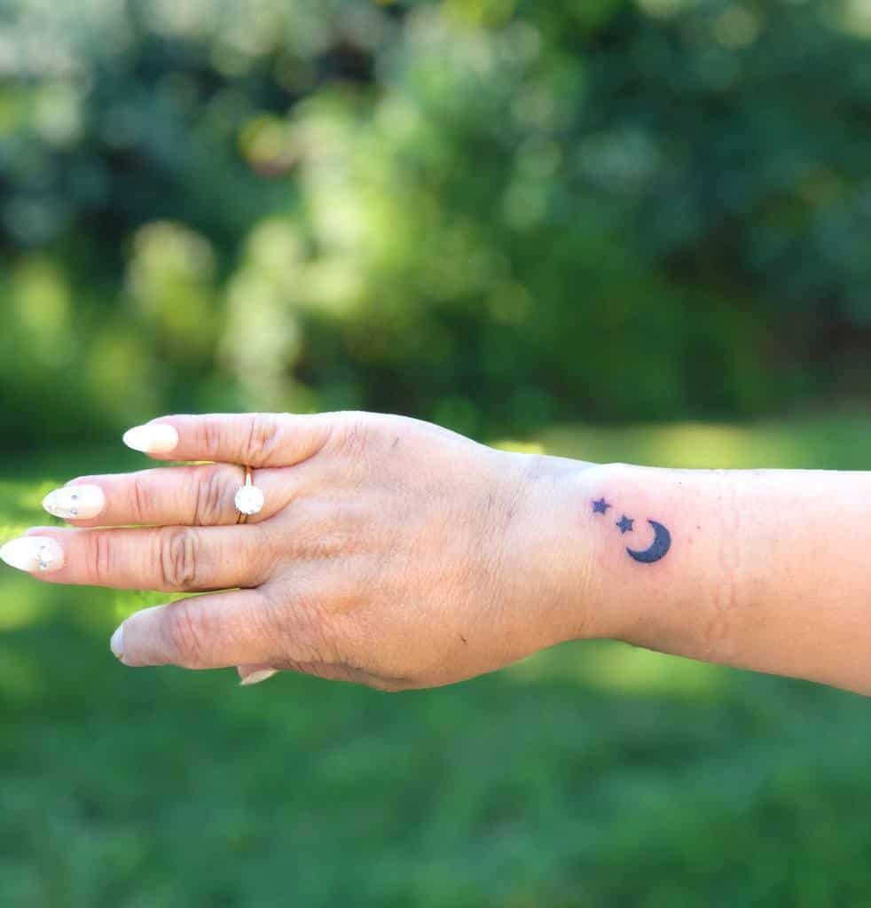 Hand with moon and stars tattoo against blurred green background