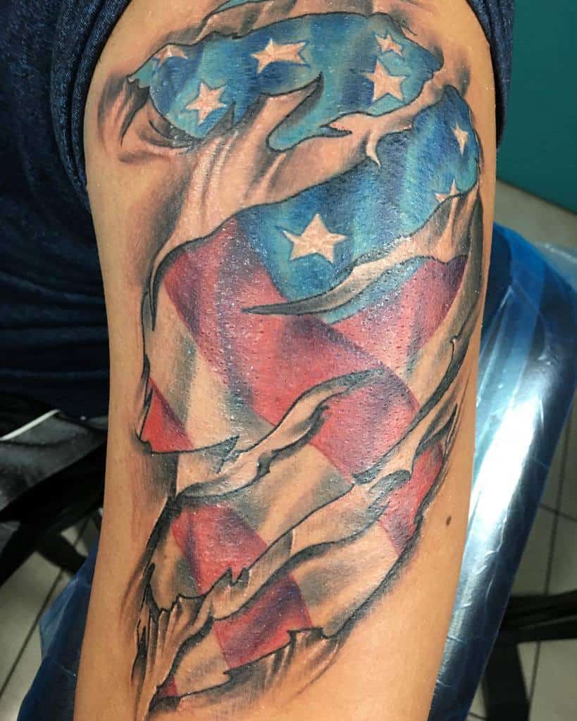 Tattoo of a tattered American flag with stars and stripes on an upper arm