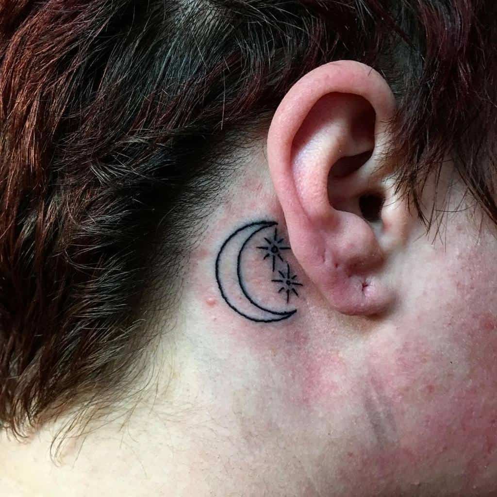 A delicate tattoo featuring a small crescent moon and stars graces the skin just behind the ear