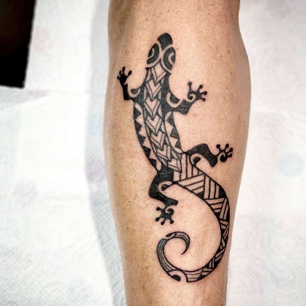 A striking tribal gecko tattoo elegantly wraps around a person's leg, showcasing intricate designs and cultural artistry