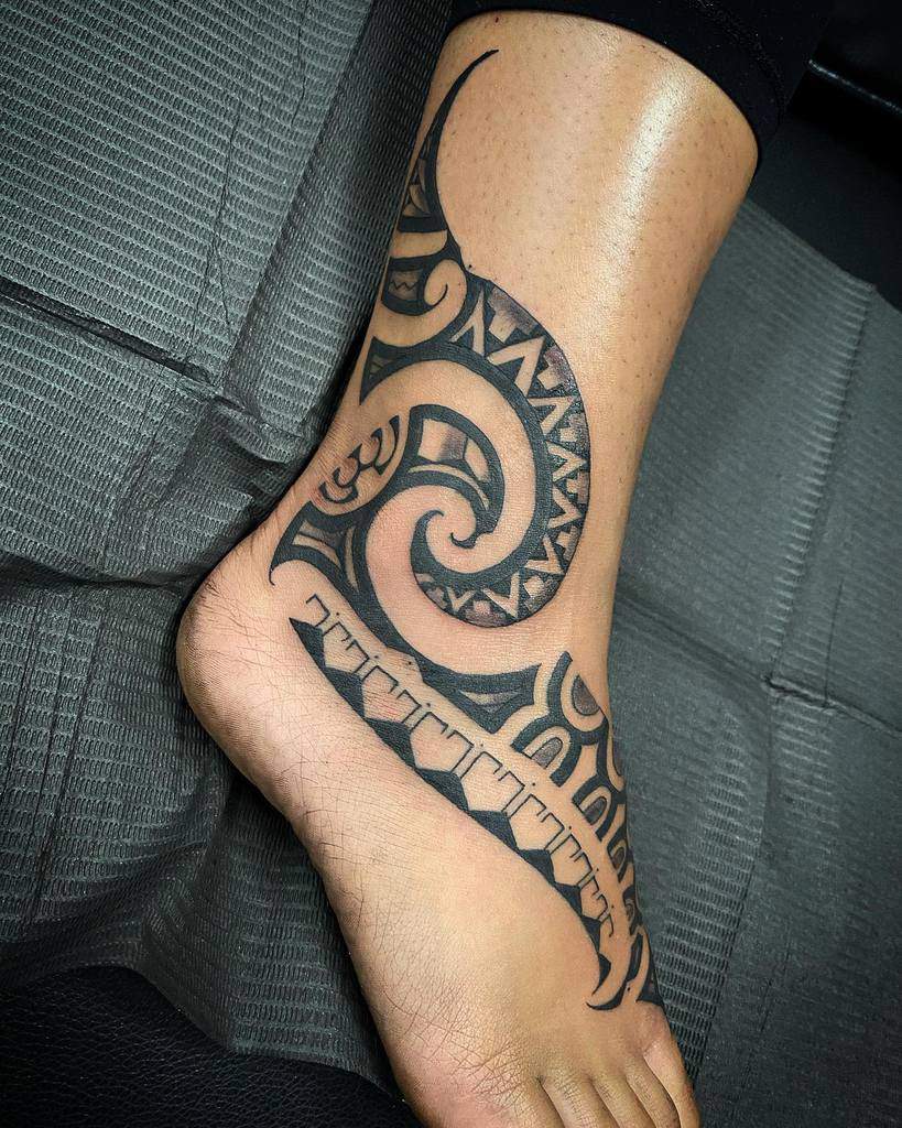 A foot adorned with an intricate tribal tattoo design wraps around the ankle and flows seamlessly down the top of the foot