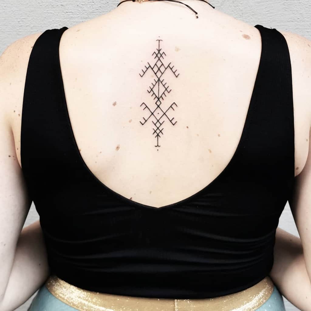 A woman with a tribal geometric tattoo on her upper back is wearing a black sleeveless top