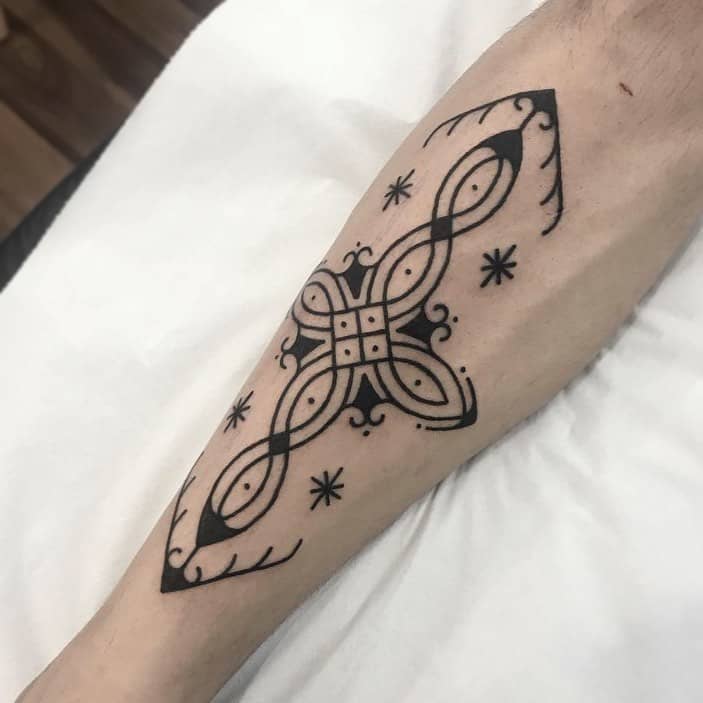 A tribal-style tattoo intricately designed with geometric and star patterns elegantly graces a person's forearm