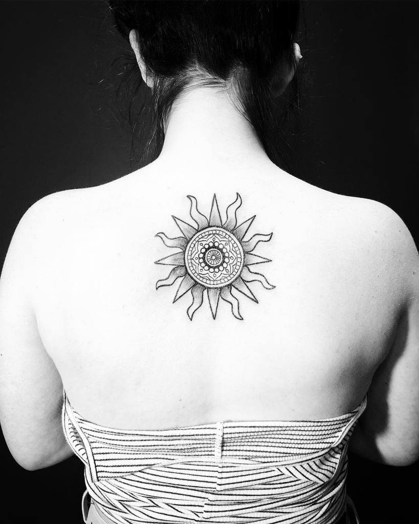 The tattoo features a detailed sun design on the upper back, with intricate geometric patterns in the center and rays extending outward, creating a bold and symmetrical tribal aesthetic