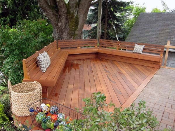 Wooden deck with built-in bench around a tree, decorative pillows, and a basket of colorful glass balls