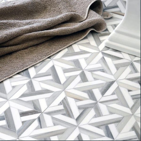 Geometric grey and white bathroom floor tiles with a folded towel nearby.