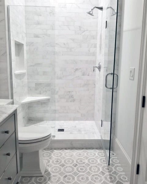 Minimalist bathroom with glass shower, marble walls, and patterned hexagonal floor tiles.