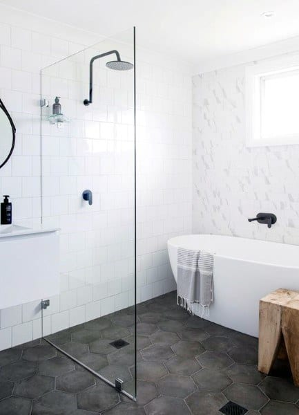 Modern bathroom with glass shower, freestanding tub, and hexagonal dark grey floor tiles.