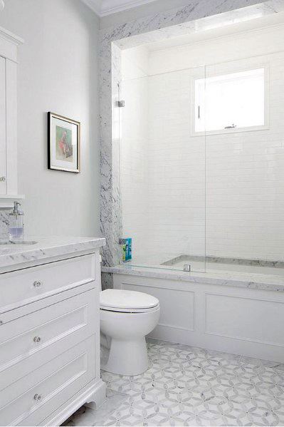 All-white bathroom with marble countertop, marble bathtub surround, and geometric floor tiles.